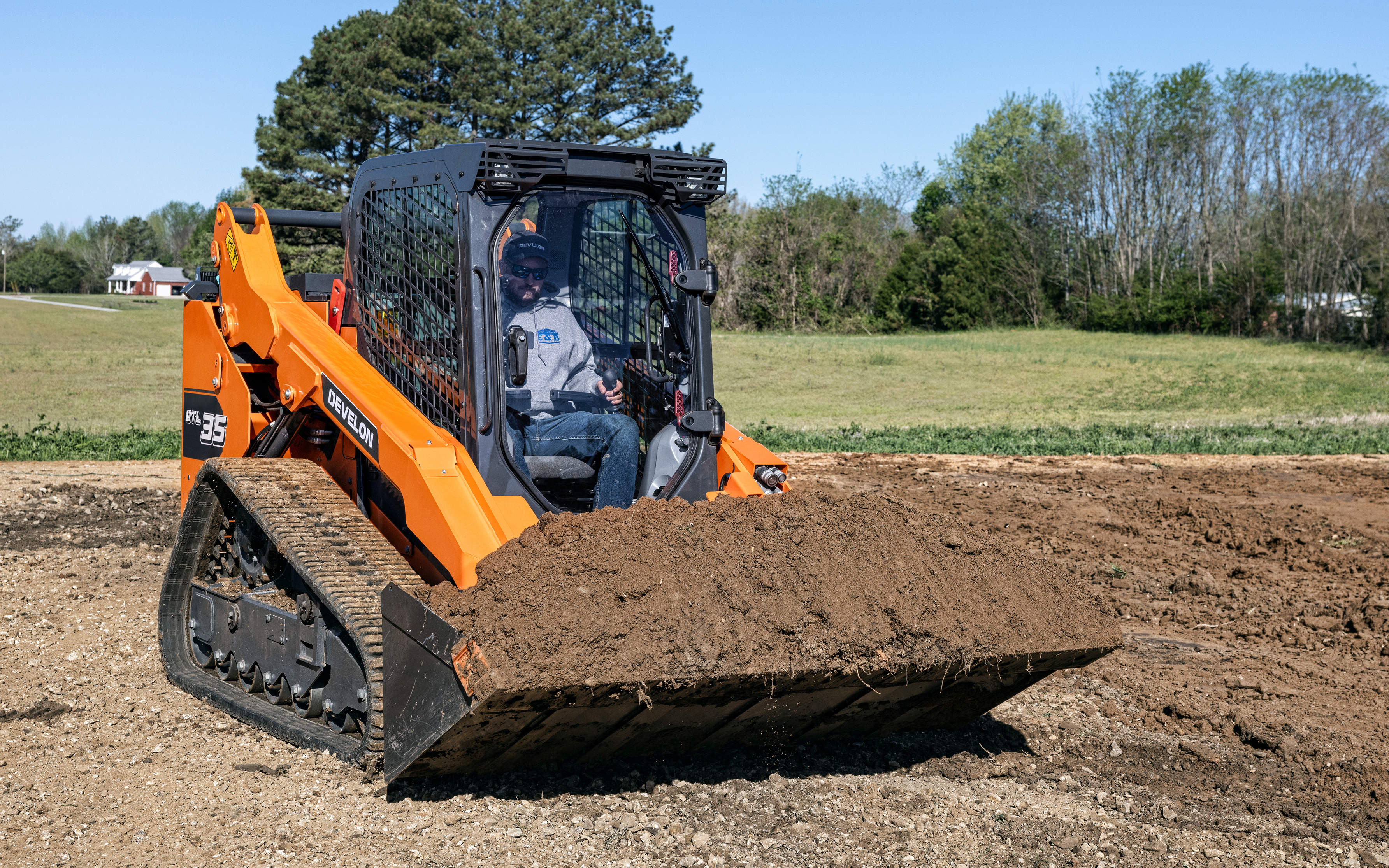 A DEVELON DTL35 compact track loader moves a full bucket of dirt.