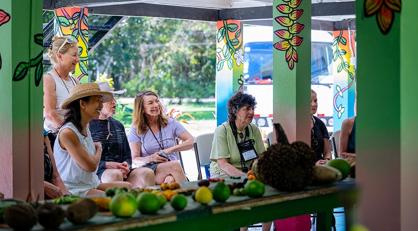 A group of Road Scholars listen to a presentation with various fruits in front of them