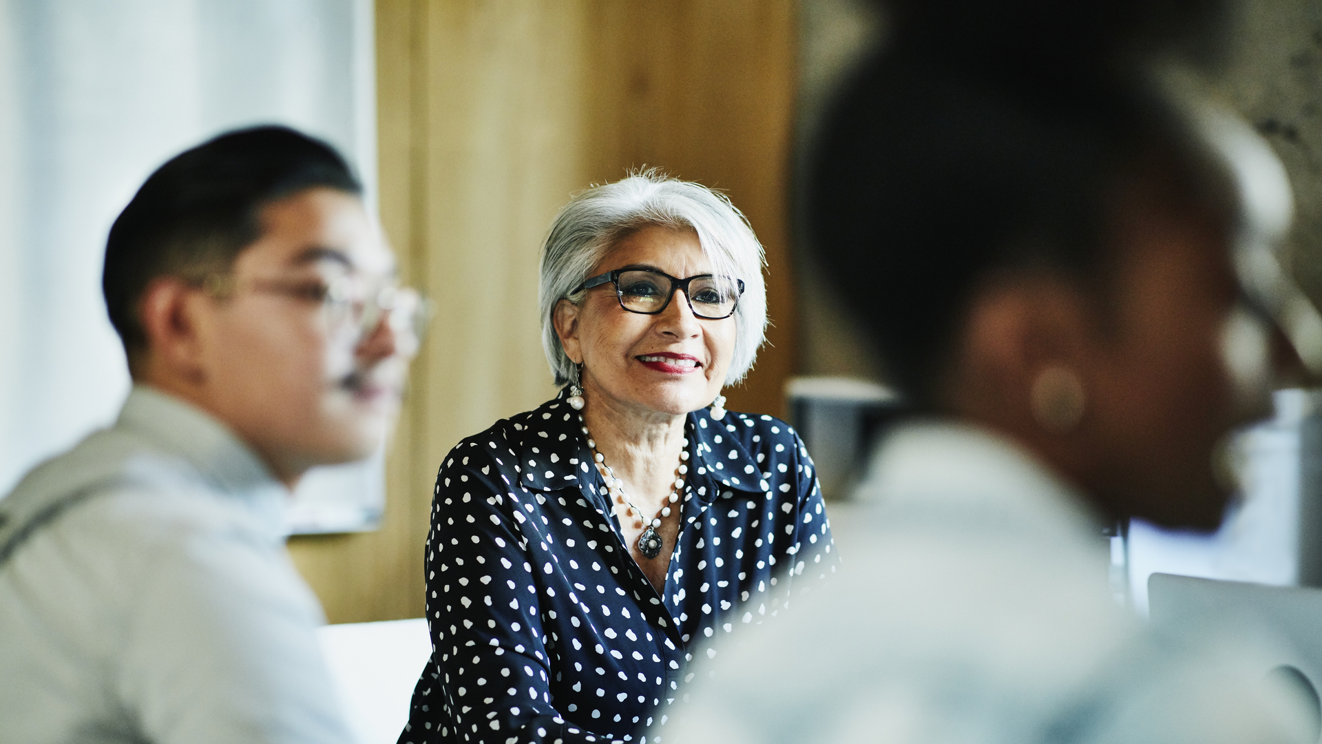 Smiling mature female business owner listening during presentation during meeting in office conference room