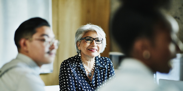 Smiling mature female business owner listening during presentation during meeting in office conference room