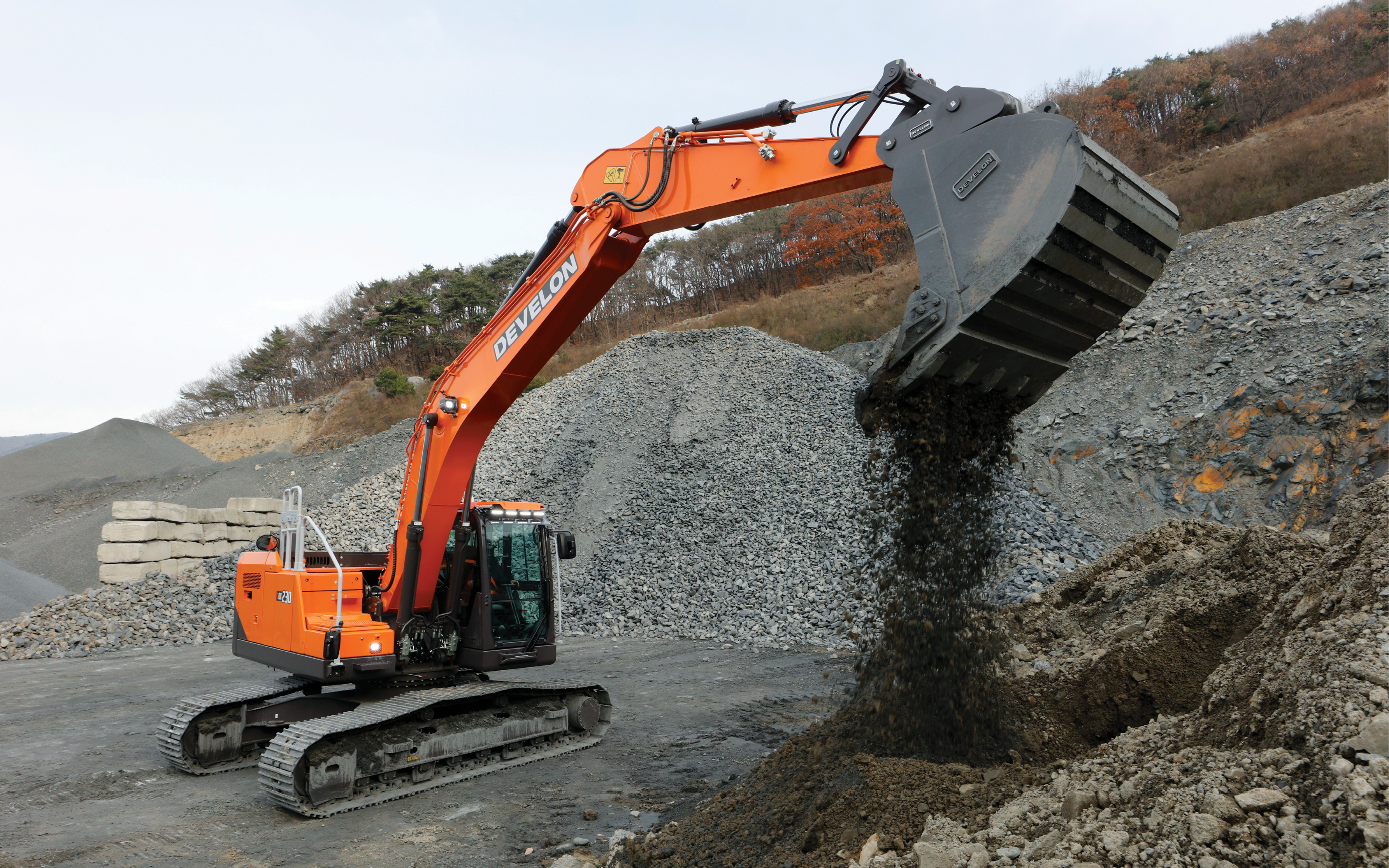 A DEVELON -9 Series excavator dumps material from its bucket on a construction job site.