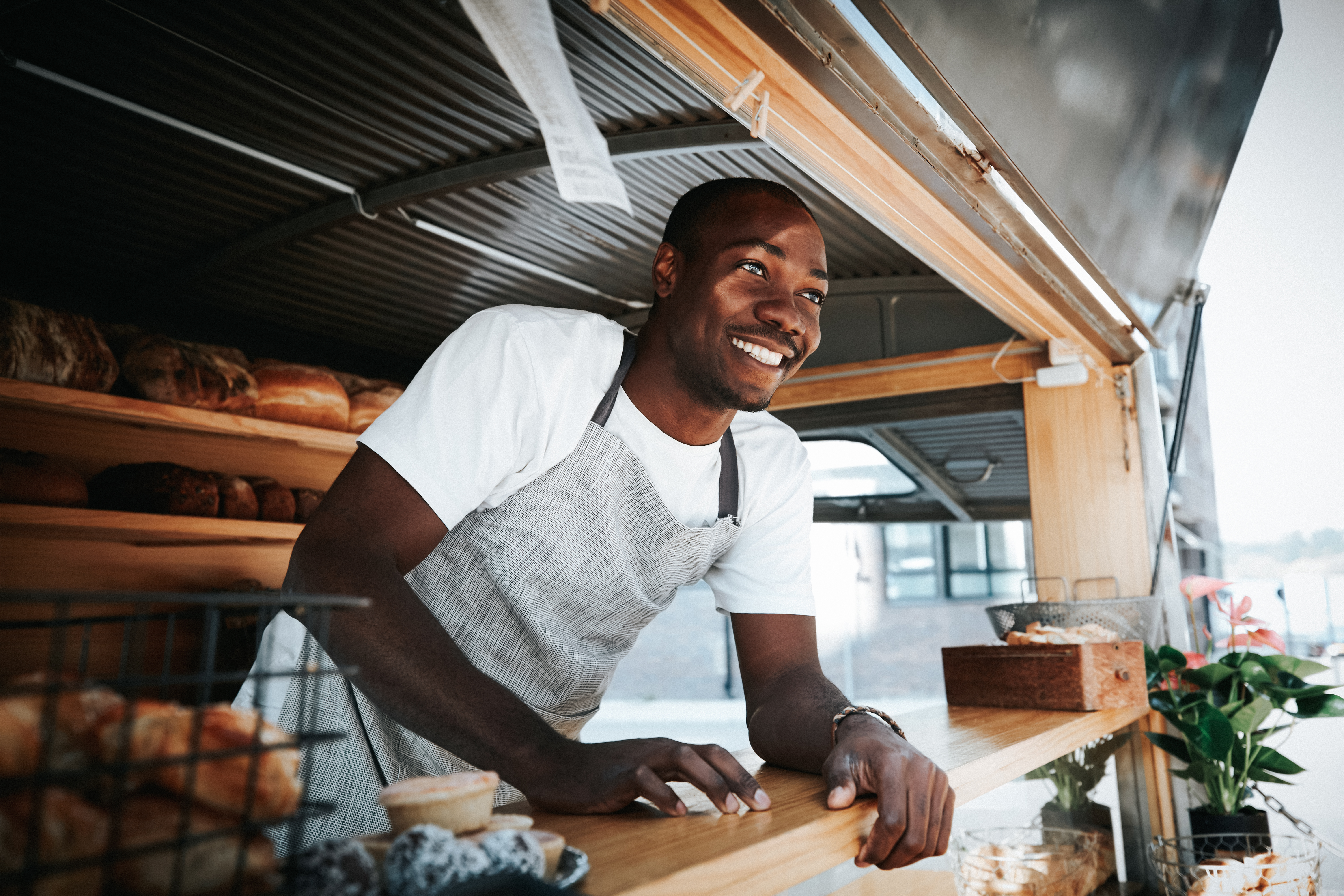 Smiling African American man leaning out of the serving window of his food truck selling baked goods 
