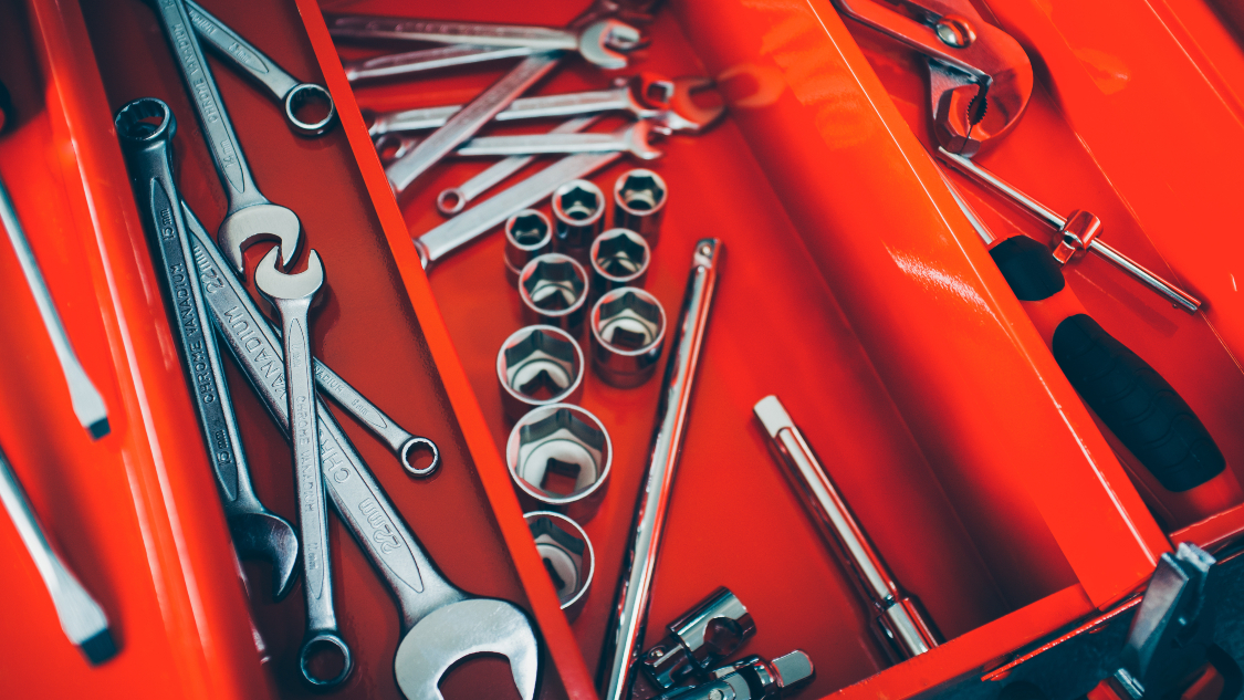 A close-up of an open red toolbox filled with various tools, including spanners, socket wrenches, screwdrivers, and ratchets. The tools are neatly arranged, indicating a well-equipped workshop or maintenance setup.