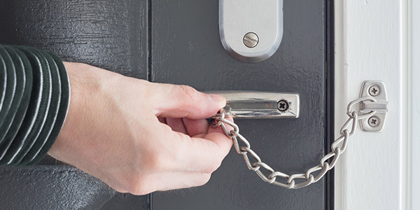 A hand closes a chain lock across a door