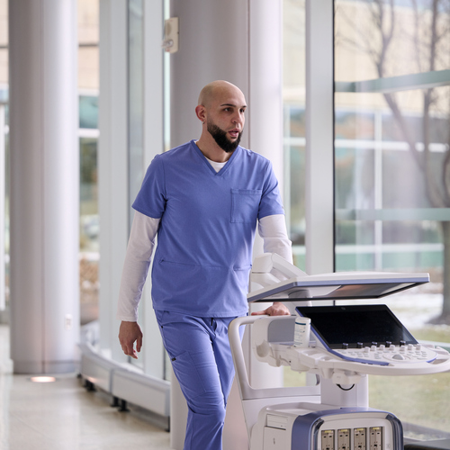 Sonographer pushes ultrasound system down a hallway