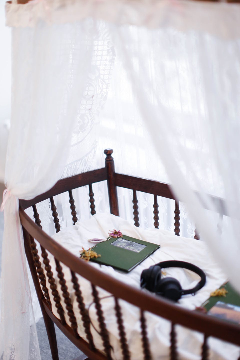 Vintage wooden crib with lace canopy, books, flowers, and headphones