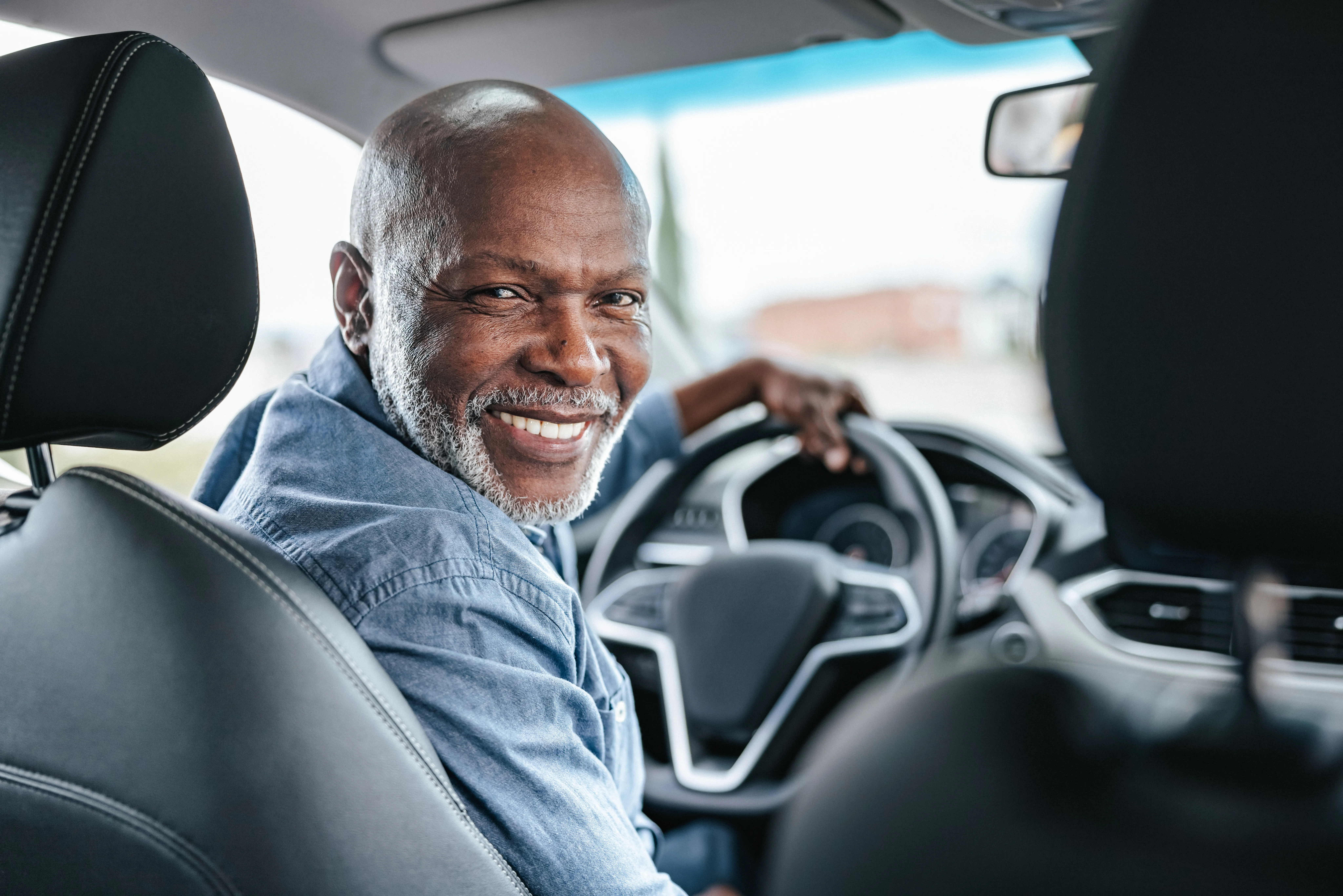 Smiling senior man in driver’s seat of a car, looking back at the passenger seat.  