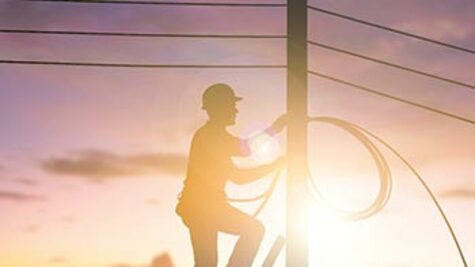 Silhouette of a technician climbing a pole to install telecommunications cabling during sunset.
