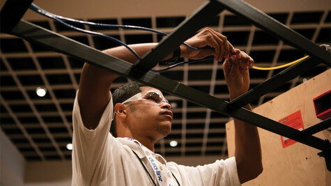 Installer wearing safety glasses routing cables through an overhead ladder rack during a hands-on training exercise