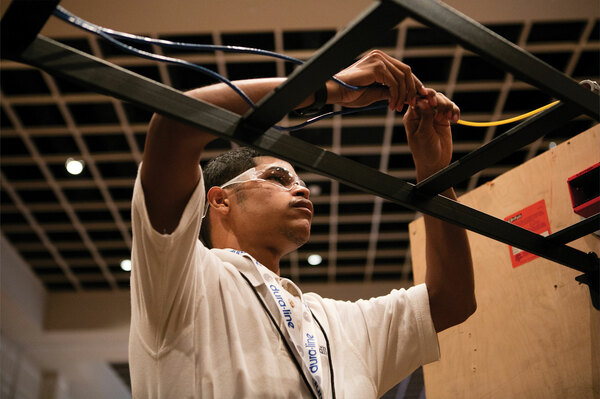 Installer wearing safety glasses routing cables through an overhead ladder rack during a hands-on training exercise