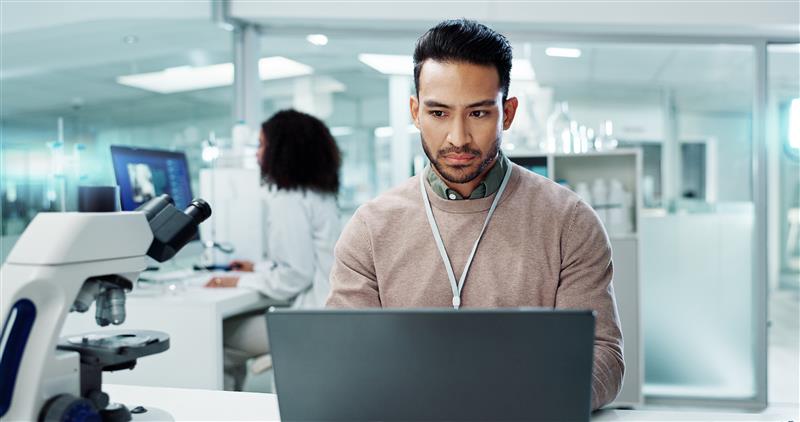 A male healthcare professional using a digital tablet at a laboratory workstation.