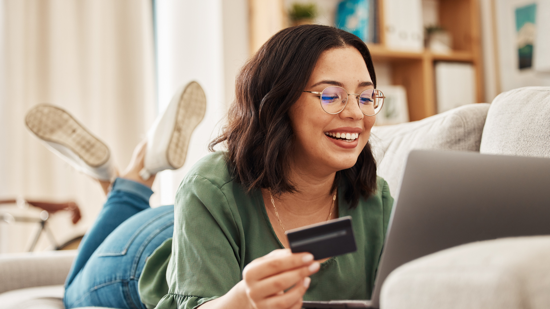 Relax, laptop and credit card, happy woman on couch in living room for internet banking in home for online shopping. Ecommerce payment, smile and cashback, girl on sofa with computer and website sale