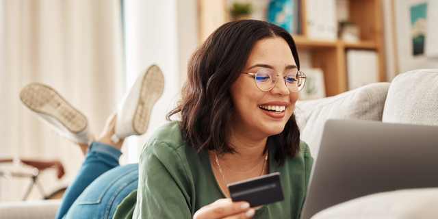 Relax, laptop and credit card, happy woman on couch in living room for internet banking in home for online shopping. Ecommerce payment, smile and cashback, girl on sofa with computer and website sale