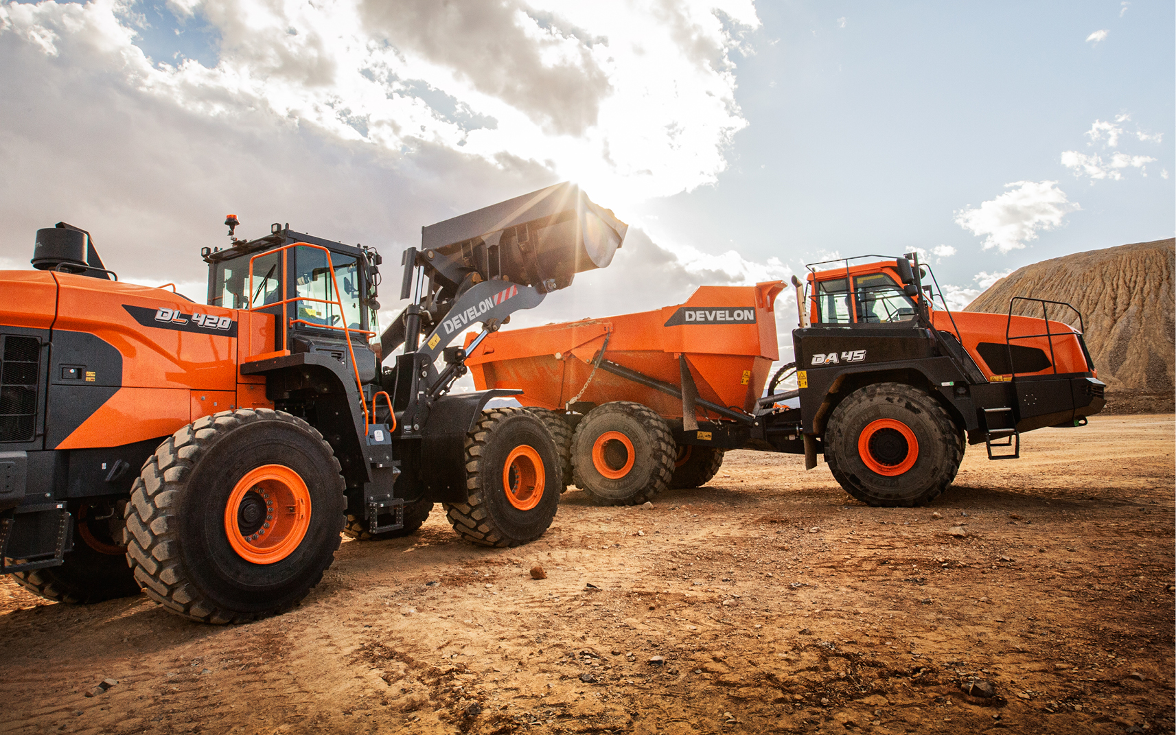 A DEVELON -7 Series wheel loader with bucket raised dumping material into the bed of an articulated dump truck.