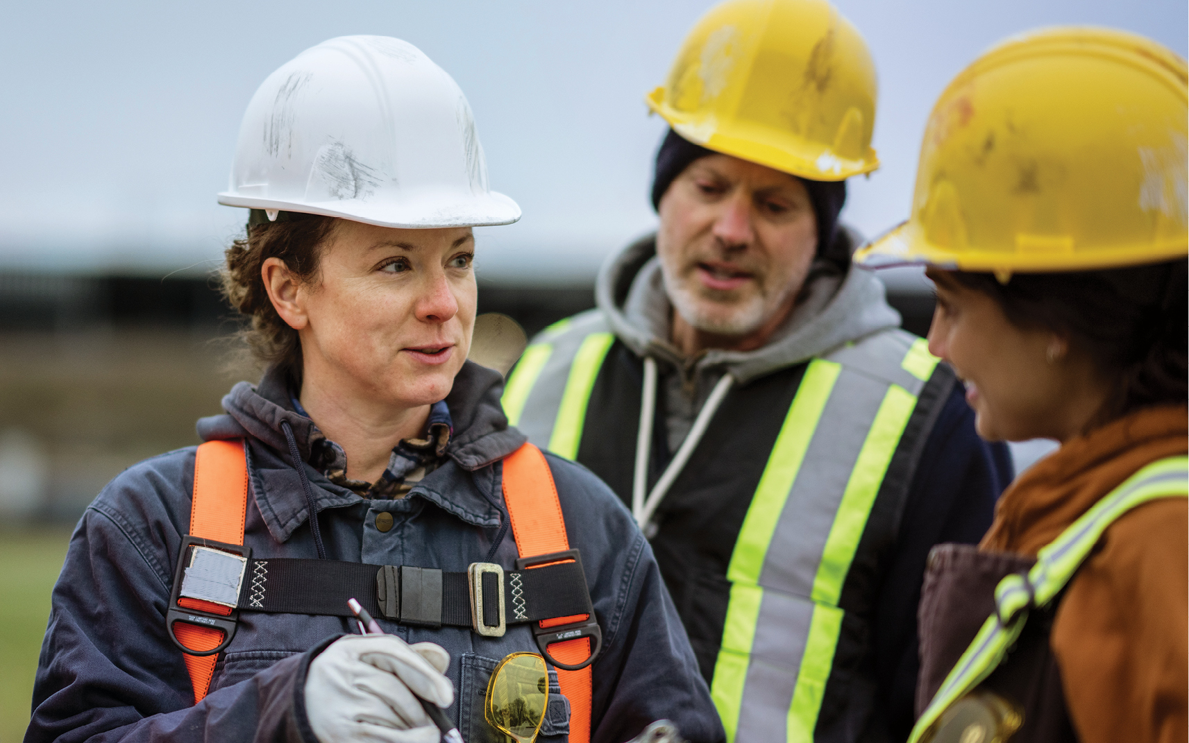 A group of construction workers wearing PPE have a conversation on a job site.