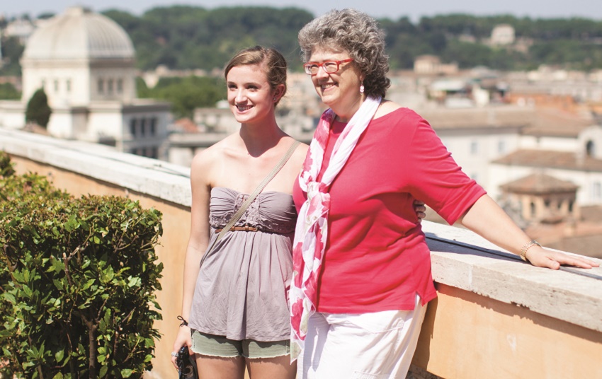 A grandparent and grandkid smile in front of a city view in Italy