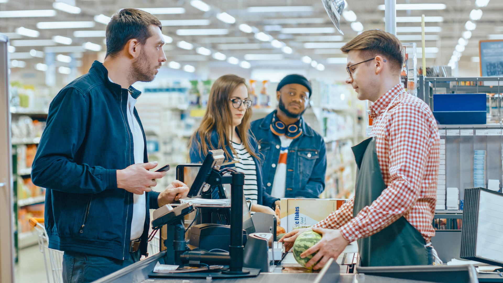 At the Supermarket: Checkout Counter Customer Pays with Smartphone for His Items. Big Shopping Mall with Friendly Cashier, Small Lines and Modern Wireless Paying Terminal System.