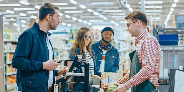 At the Supermarket: Checkout Counter Customer Pays with Smartphone for His Items. Big Shopping Mall with Friendly Cashier, Small Lines and Modern Wireless Paying Terminal System.