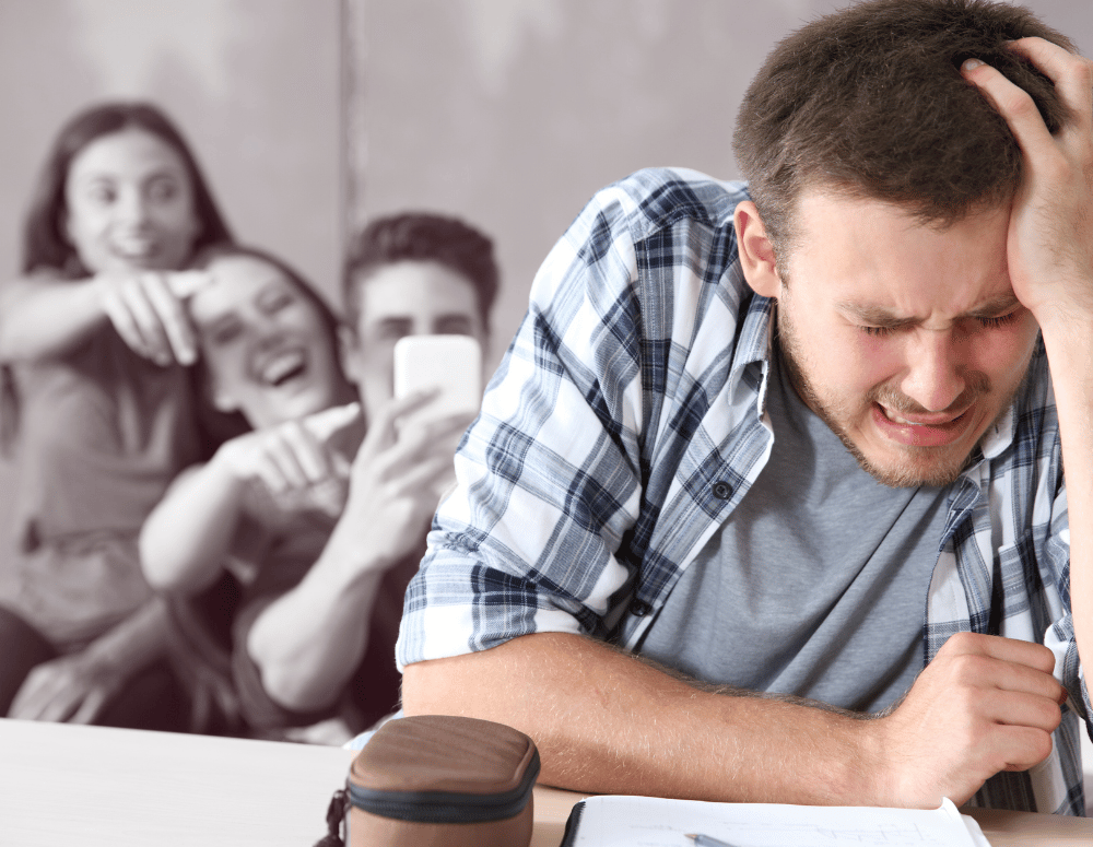 Teen boy looks upset while other students film him and laugh.