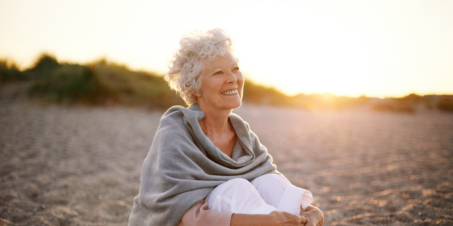 Cheerful old woman sitting on the beach