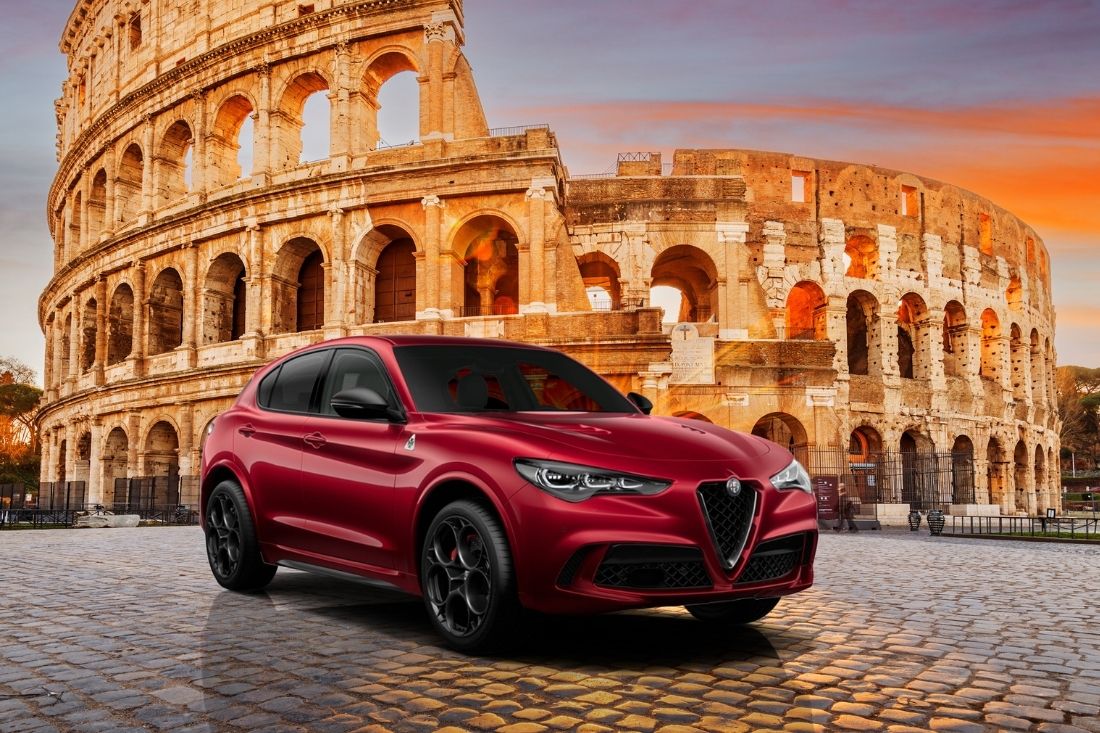 A red Alfa Romeo Stelvio Quadrifoglio parked in front of the Roman Colosseum.