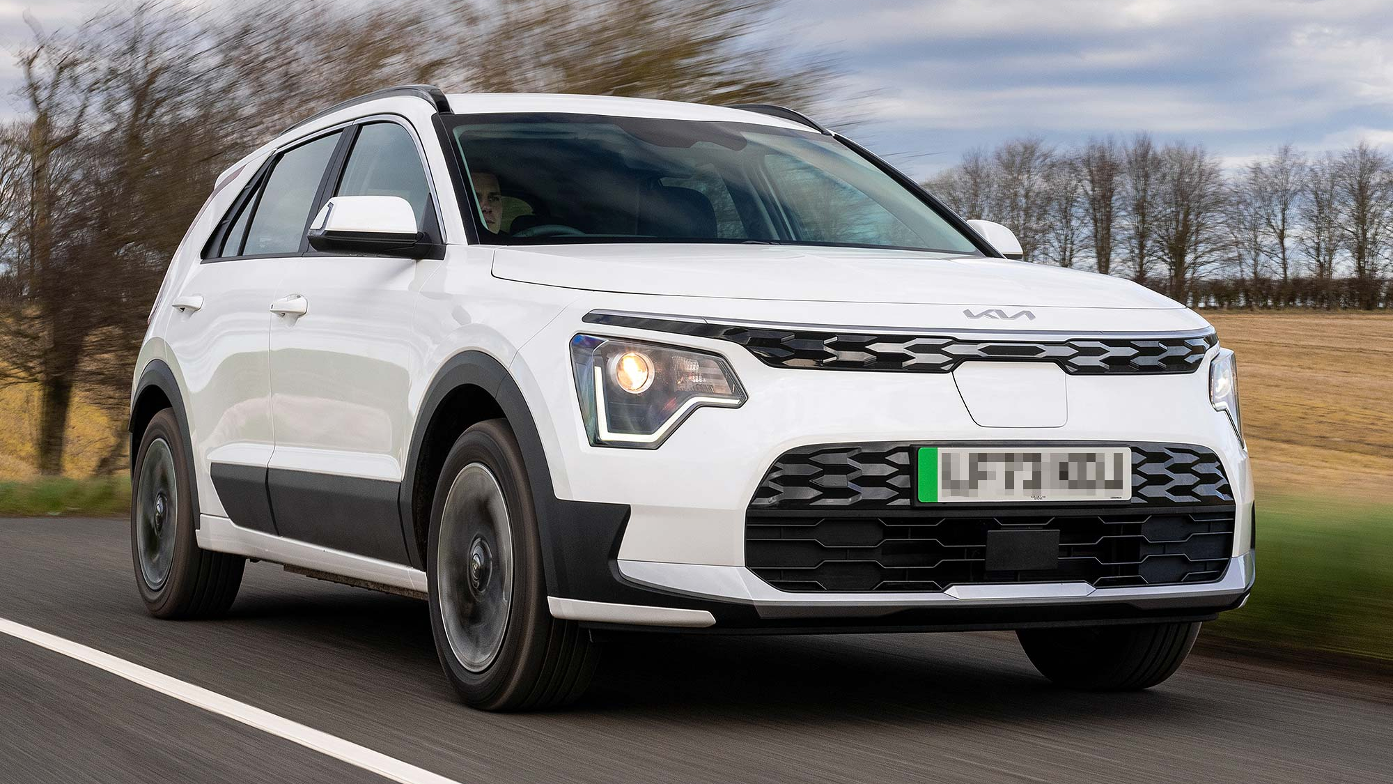 White Kia Niro electric SUV driving on a country road, available on the Motability Scheme