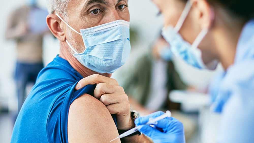 Image of a doctor vaccinating a male patient. Both are masked