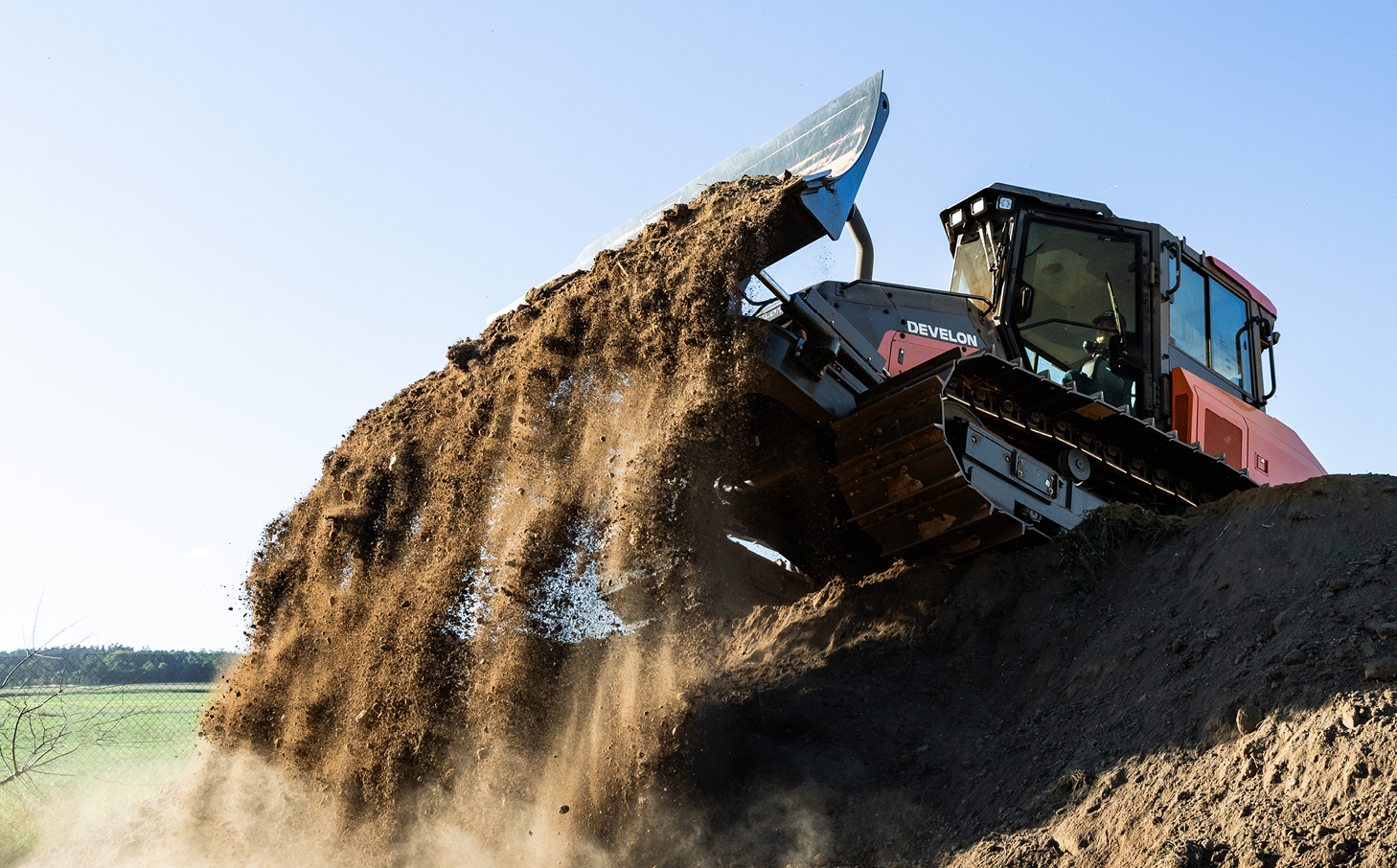 A DEVELON dozer pushing dirt on farmland.
