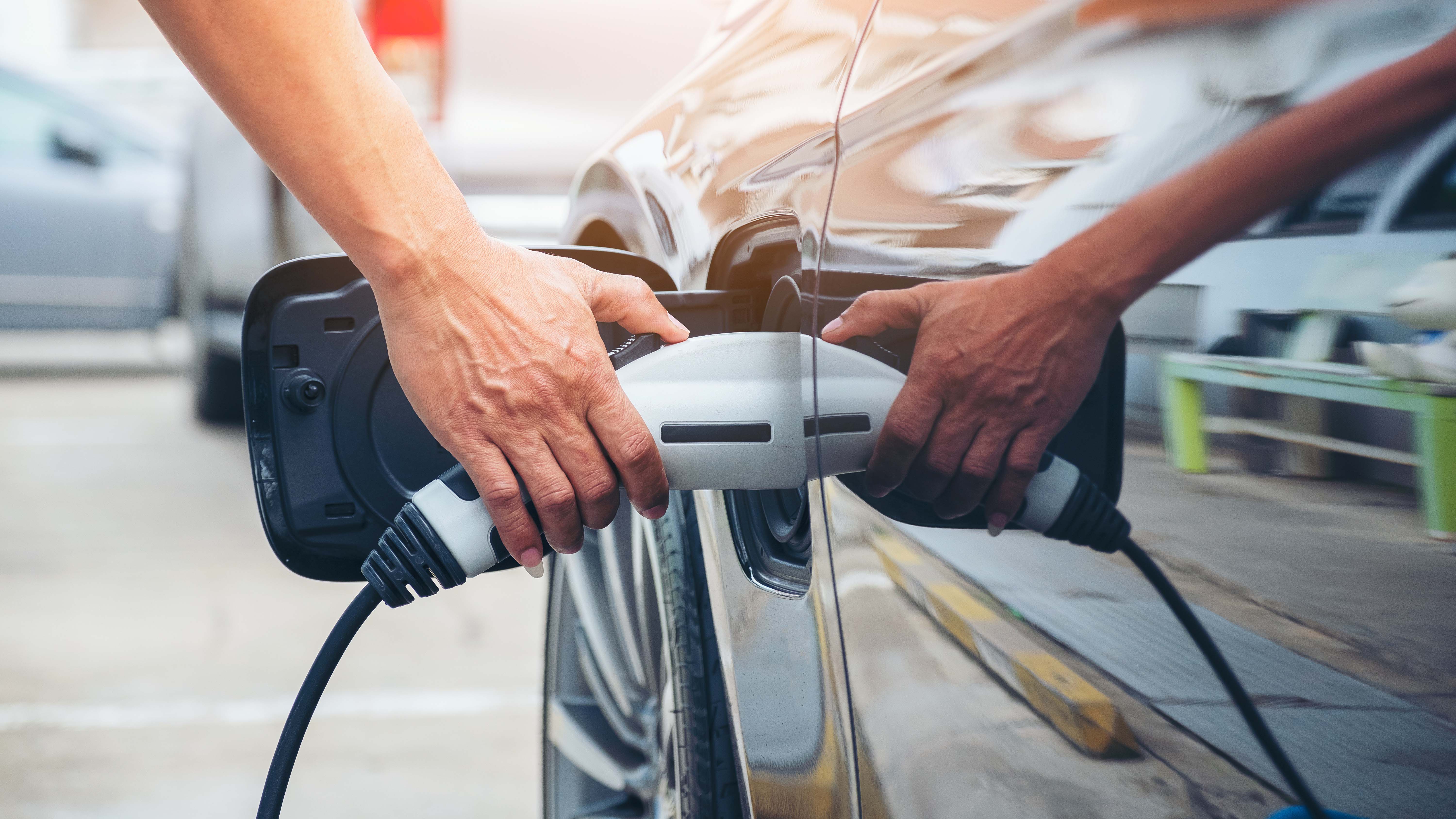 A hand holding an EV charger plugged into an EV