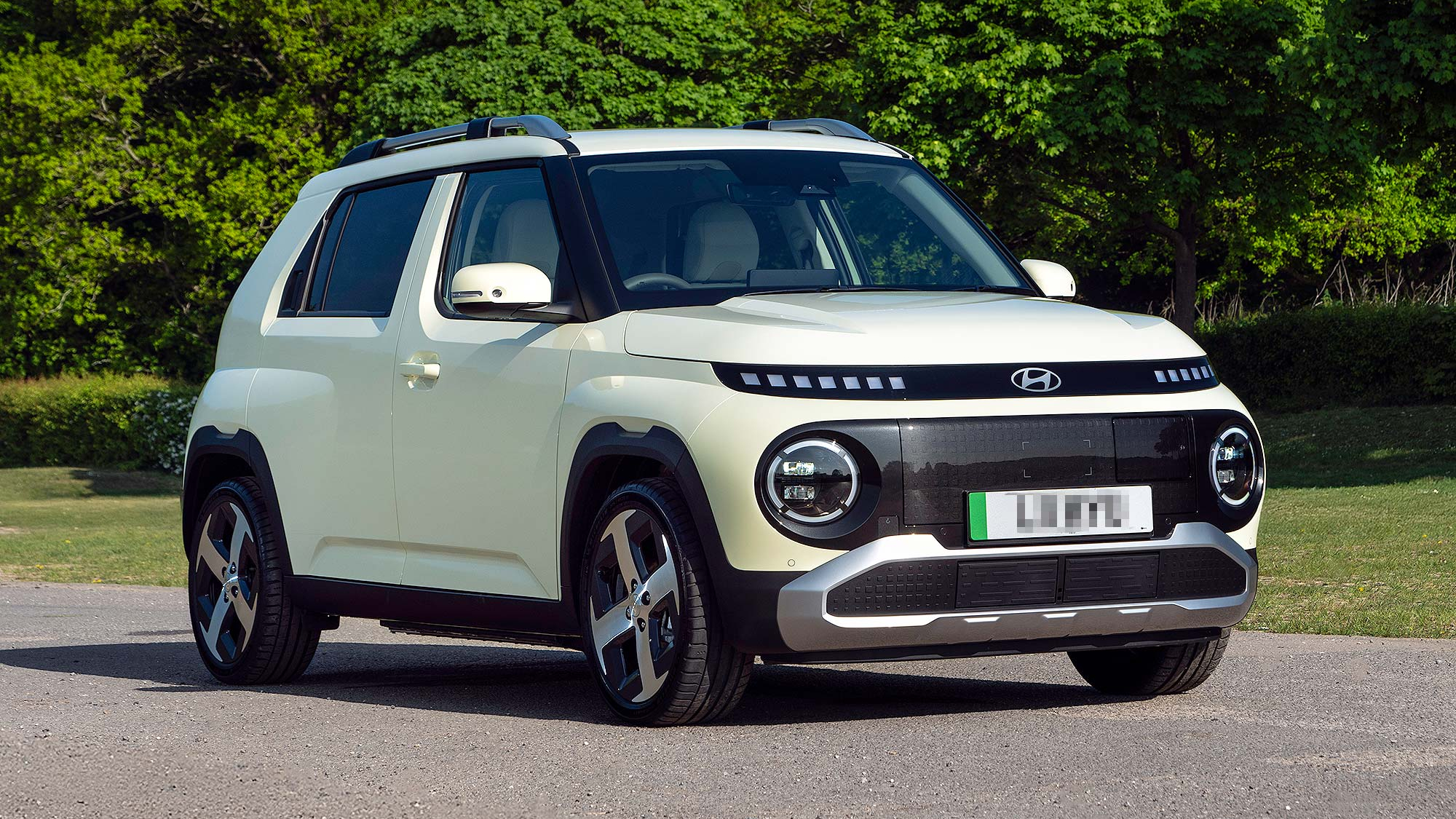 A cream-coloured Hyundai Inster EV parked on a sunny roadside, showcasing its bold, boxy shape with round headlights and futuristic styling.