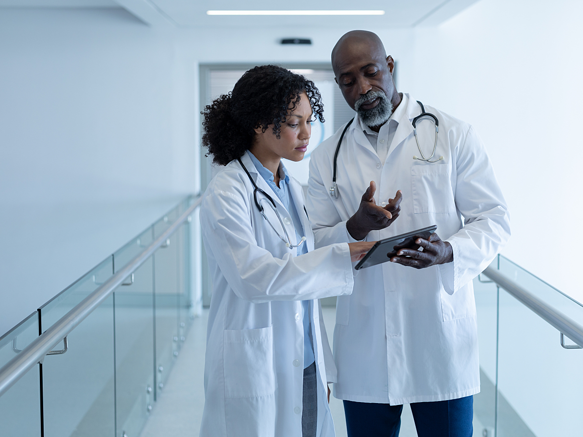 Diverse male and female doctor talking seriously and looking at digital tablet in hospital corridor. medicine, health and healthcare services.