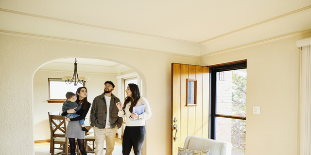 Wide shot of family looking at home for sale with real estate agent