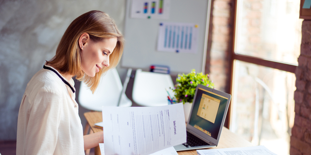 Cute young blond lady is concentreted on ideas for new start up. She is in casual shirt, sitting at her work place and studying documents