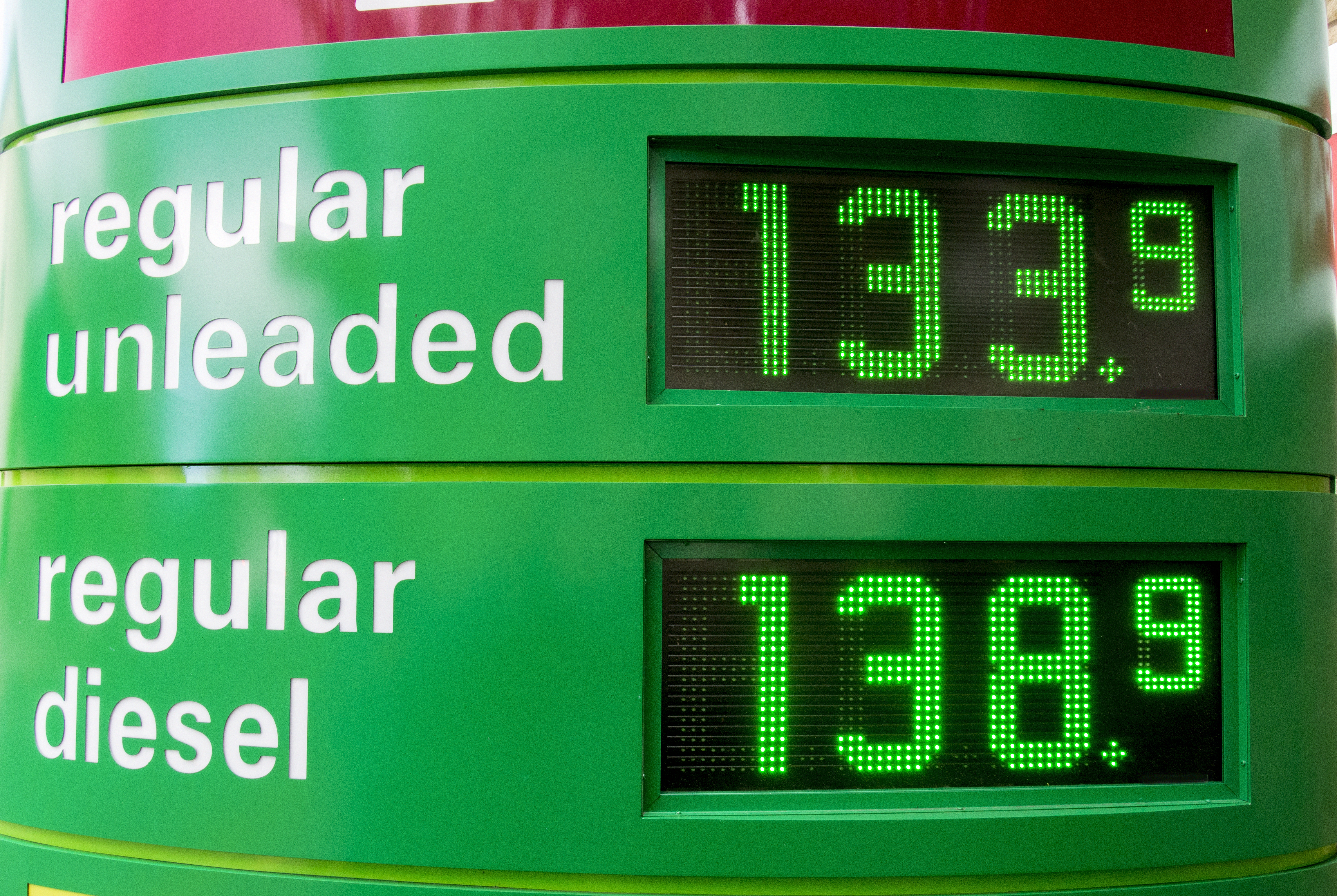 A green digital fuel price display at a petrol station shows regular unleaded at 133.9 and regular diesel at 138.9.