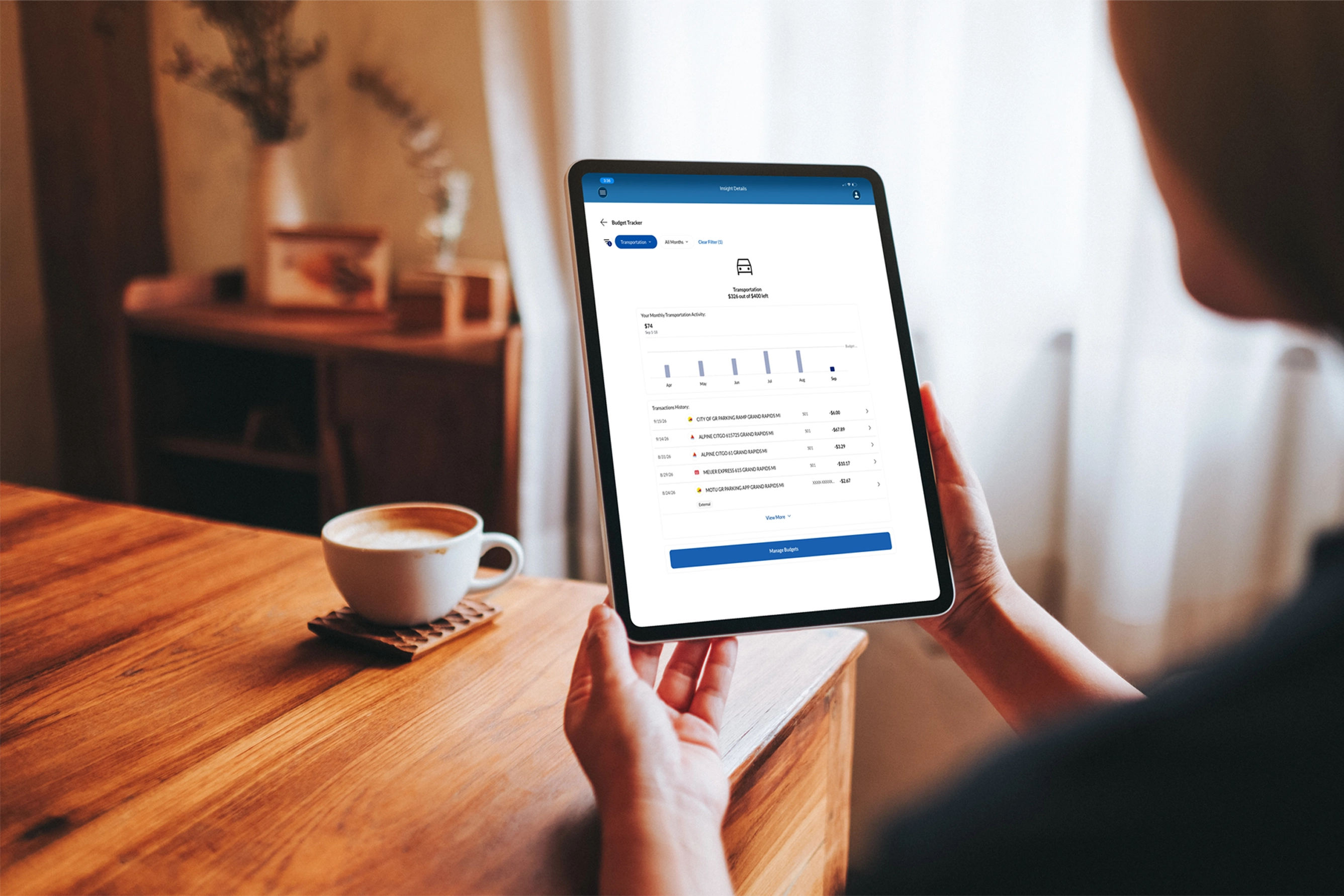 Person using a tablet to review budget tracking and spending activity at a table with a coffee cup nearby.