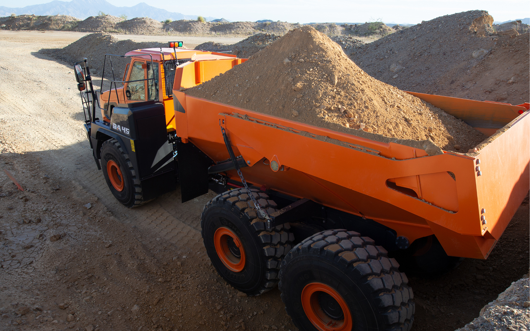 A DEVELON articulated dump truck carries material on a construction job site.