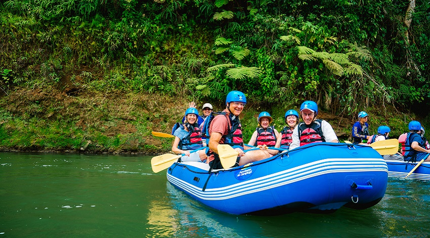 A group smiles from a blue raft in the middle of a river in Costa Rica
