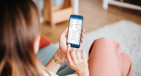 Woman sitting on a comfortable sofa, browsing LMCU Mobile App on phone    