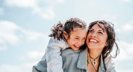 Smiling woman carrying her smiling young daughter on her back on a bright sunny day 