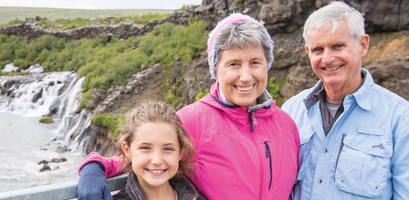 A smiling girl with her grandparents stand in front of a waterfall in Iceland.