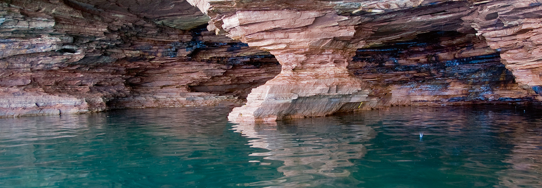 Layered sandstone formations create a sea cave with a pillar over the teal water of Apostle Islands National Lakeshore in Wisconsin.