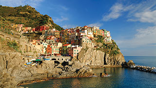 The colorful village of Manarola in Cinque Terre, Italy, built on a cliff overlooking the Mediterranean Sea under a blue sky.