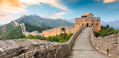 The Great Wall of China winds over lush green hills with a watchtower under a colorful sky.