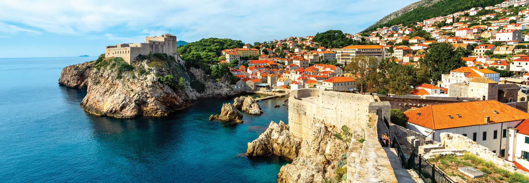 A medieval fortress and red-roofed city in the Balkans meets the stunningly blue Adriatic Sea on a sunny day.