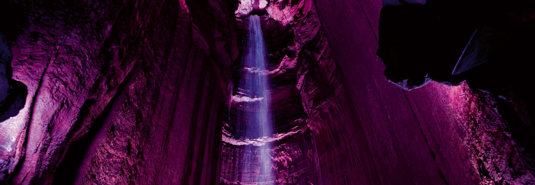 A waterfall inside a cavern in Tennessee is illuminated by vibrant purple lights as it cascades down through the darkness.
