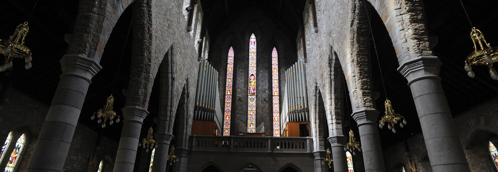 The interior of a grand stone church in Ireland, with large pillars, stained-glass windows, and a large pipe organ.