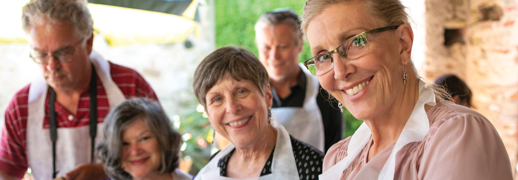 A group of smiling people in aprons participate in a cooking class in Tuscany, Italy.