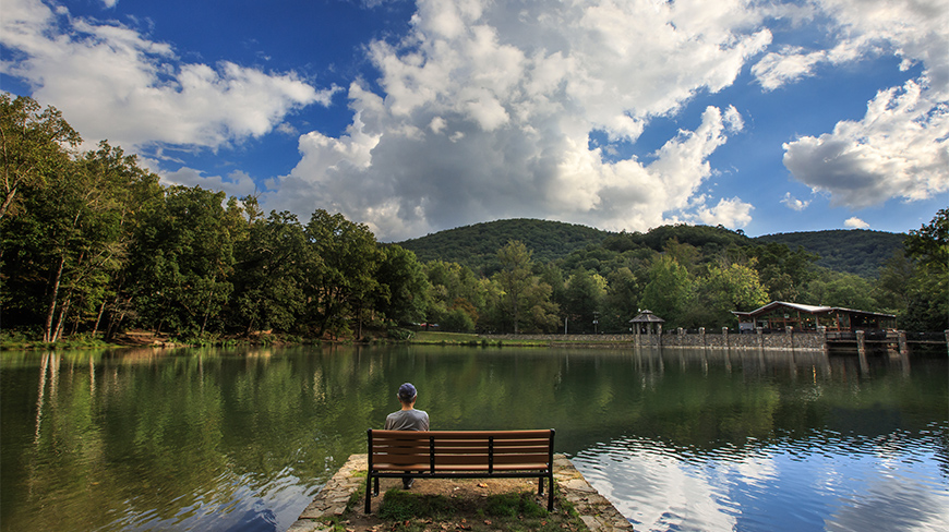 A person sits on a bench looking out at the lake and mountains at the Montreat Conference Center in North Carolina.