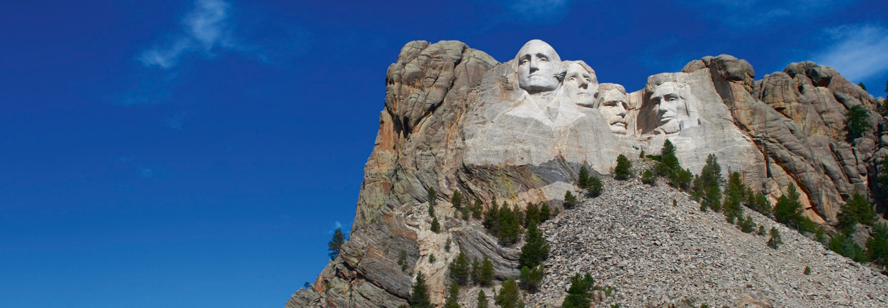 The granite-carved faces of four presidents at Mount Rushmore in South Dakota under a brilliant blue sky.