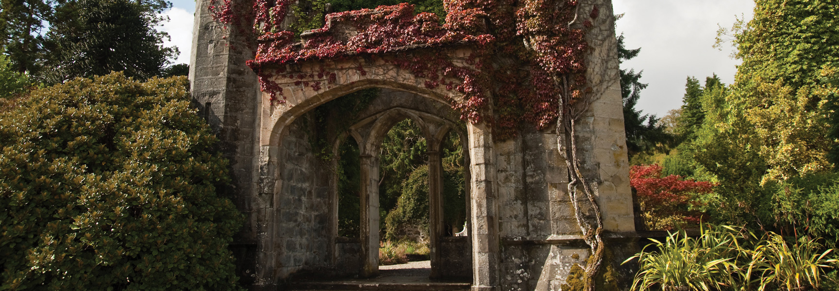 An old stone archway covered in red ivy stands in a lush garden in the Scottish Highlands.